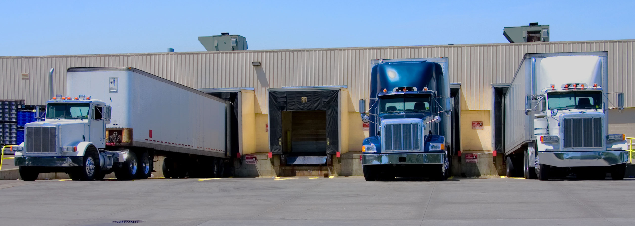 Three semi trucks backed up to loading dock of warehouse