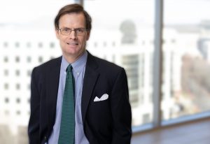 Allen Smith wearing a dark suit and striped green tie