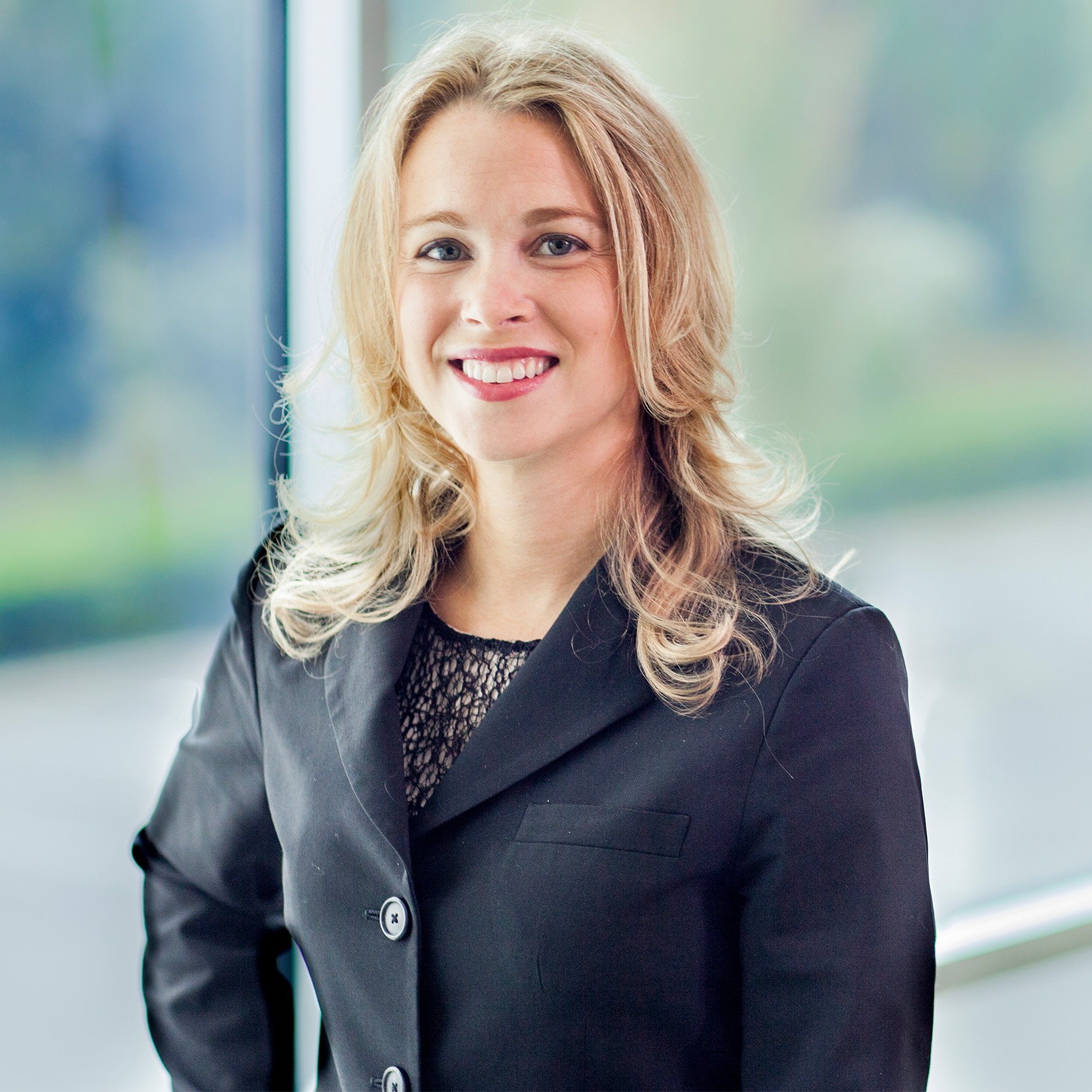 Kari standing front of a window wearing a black suit and black blouse.