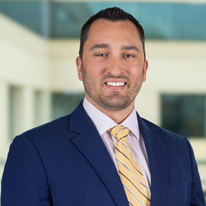 Jesse standing and facing camera with dark blue suit and gold tie