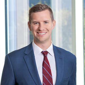 Ryan Mitiguy wearing a navy blazer and red striped tie.